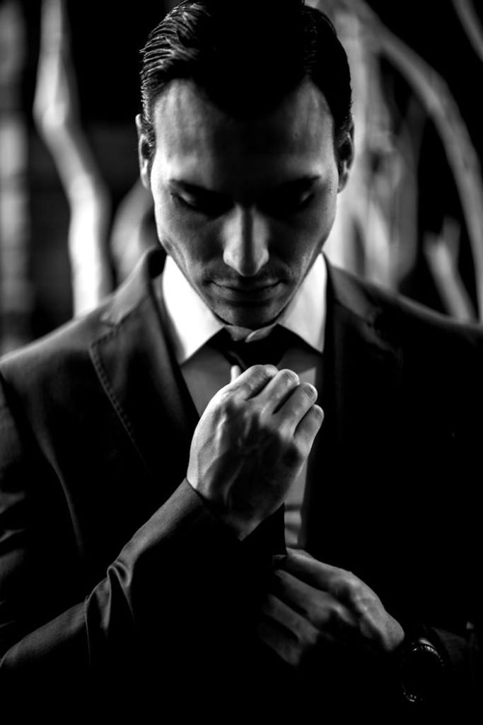 Professional black and white portrait of a man adjusting his necktie in a suit.