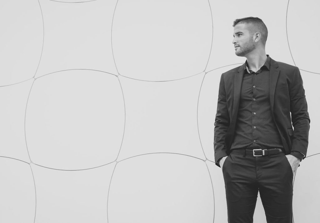 Black and white portrait of a confident man in a suit looking sideways against a geometric background.